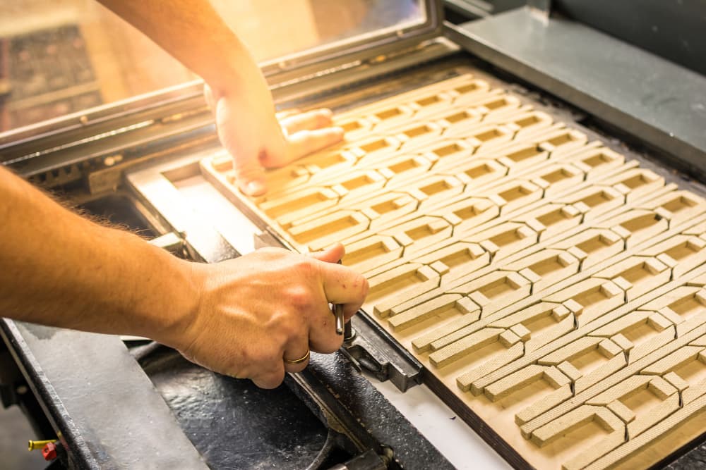 Mani che lavorano con una fustella in legno per il taglio di forme geometriche ripetute.